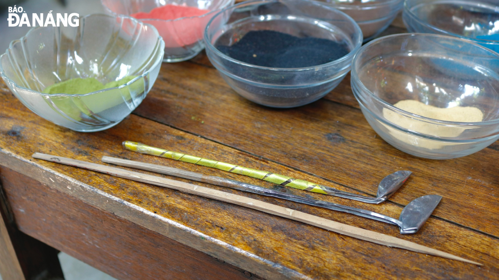 Dung's sand painting tools are homemade from stainless steel spoons and bamboo sticks, including a sand pouring tool and a sharpened bamboo stick called a drawing pen.