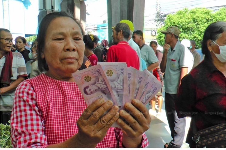 A woman holds up her share of the 10,000-baht cash handout, which is deemed part of the government's economic stimulus plan. (Photo: Bangkokpost)