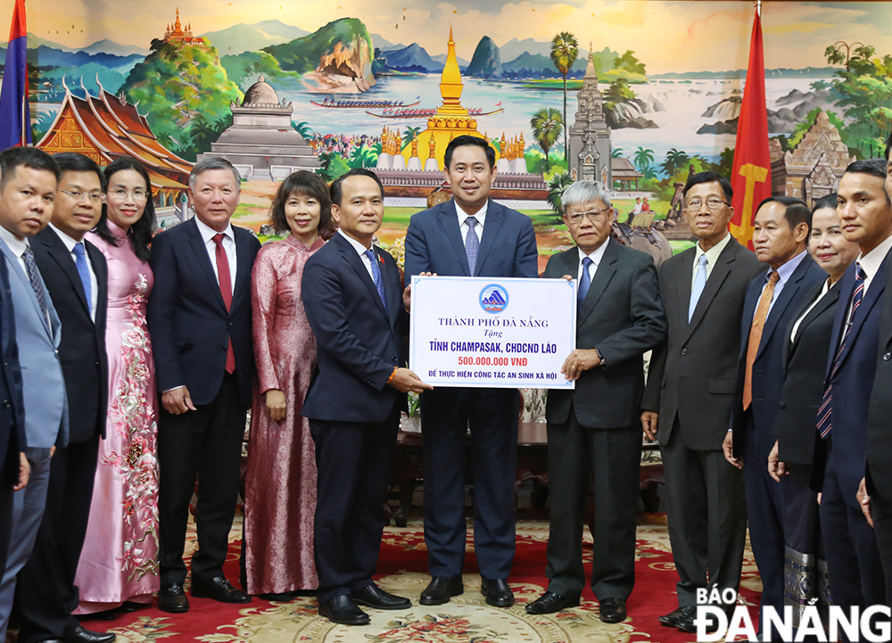 Phó Bí thư Thường trực Thành ủy Nguyễn Đình Vĩnh (thứ 6 từ trái qua) trao bảng tượng trưng tặng số tiền 500 triệu đồng hỗ trợ tỉnh Champasak thực hiện công tác an sinh xã hội. Ảnh: ĐẮC MẠNH