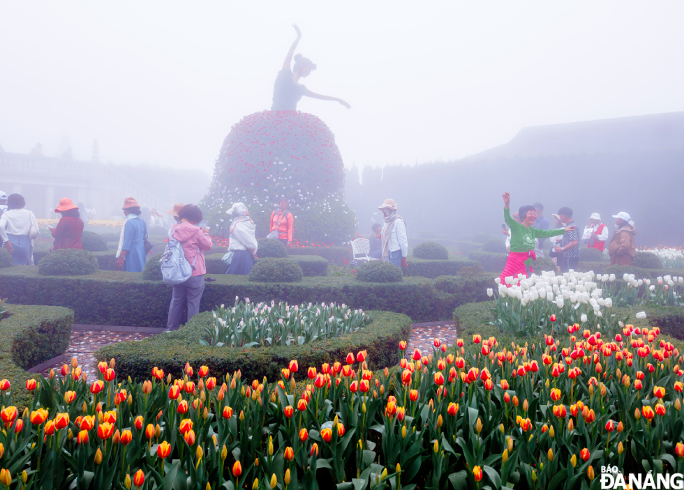 The graceful statue of a young woman extending her hand amidst the vibrant tulip garden, shrouded in the mist characteristic of Ba Na Hills, creates a scene full of mystery and romance.